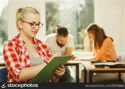 Education, high school, teamwork and people concept - student girl with notebook sitting in front of students her group mates in classroom. Student girl in front of her mates in classroom
