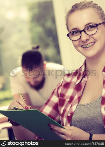 Education, high school, teamwork and people concept - student girl with notebook sitting in front of students her mates in classroom. Student girl in front of her mates in classroom