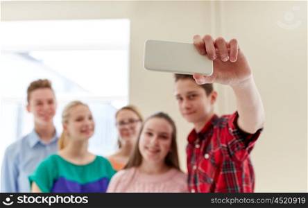 education, high school, technology and people concept - group of happy smiling students taking selfie picture with smartphone in corridor