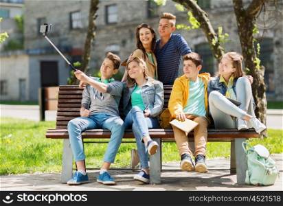 education, high school, technology and people concept - group of happy teenage students or friends taking selfie by smartphone and monopod