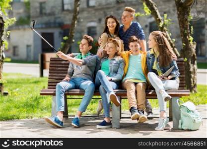 education, high school, technology and people concept - group of happy teenage students or friends taking selfie by smartphone and monopod