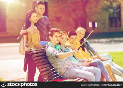 education, high school, technology and people concept - group of happy teenage students or friends taking selfie by smartphone and monopod. happy teenage students taking selfie by smartphone