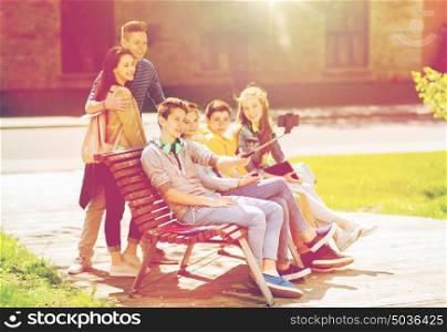 education, high school, technology and people concept - group of happy teenage students or friends taking selfie by smartphone and monopod. happy teenage students taking selfie by smartphone