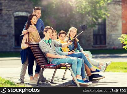 education, high school, technology and people concept - group of happy teenage students or friends taking selfie by smartphone and monopod. happy teenage students taking selfie by smartphone. happy teenage students taking selfie by smartphone