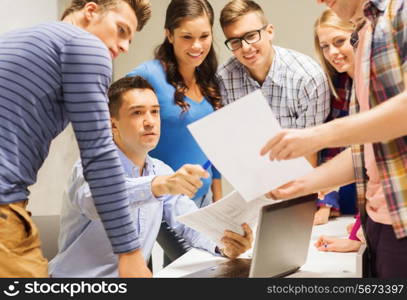 education, high school, technology and people concept - group of smiling students and teacher with papers, laptop computer in classroom