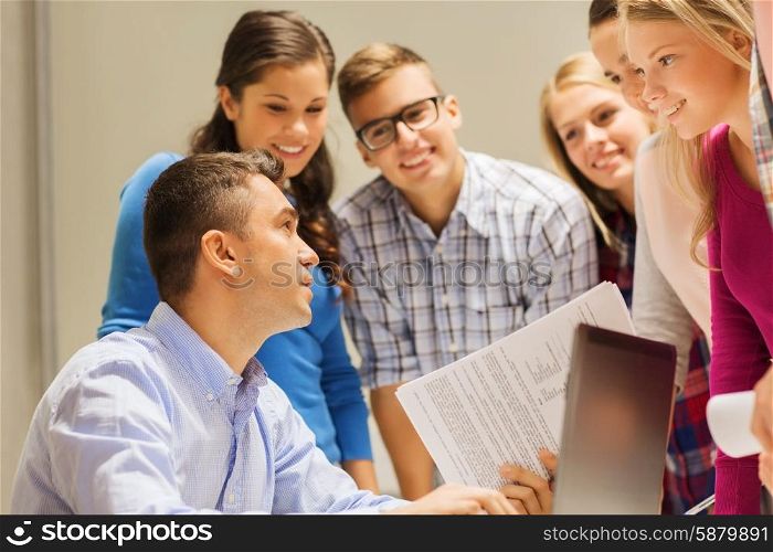 education, high school, technology and people concept - group of smiling students and teacher with papers, laptop computer in classroom