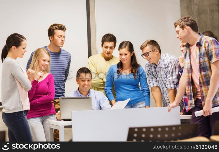 education, high school, technology and people concept - group of smiling students and teacher with papers, laptop computer in classroom