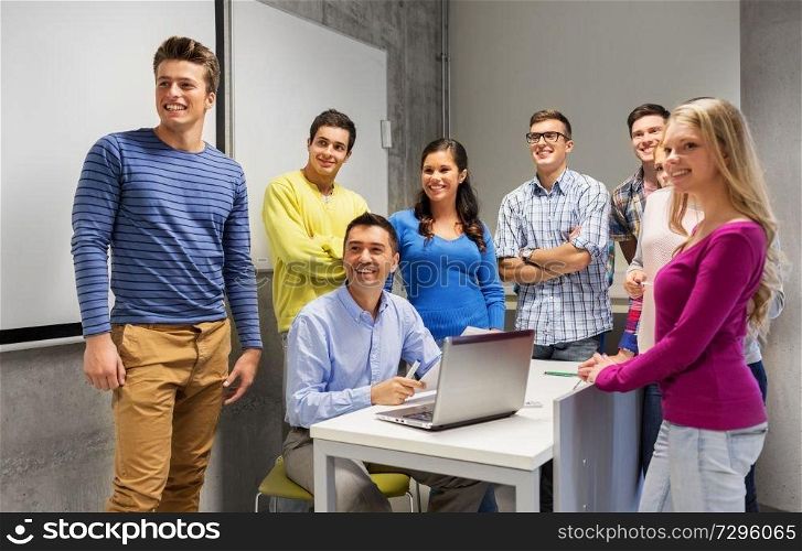 education, high school, technology and people concept - group of students and teacher with papers and laptop computer in classroom. students and teacher with papers and laptop