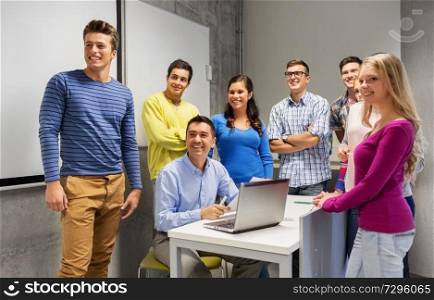 education, high school, technology and people concept - group of students and teacher with papers and laptop computer in classroom. students and teacher with papers and laptop