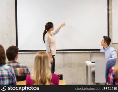 education, high school, technology and people concept - smiling student girl standing in front of white board and teacher with laptop computer in classroom