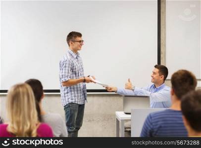 education, high school, technology and people concept - smiling student with notepad, laptop computer standing in front of teacher showing thumbs up gesture in classroom
