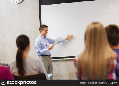 education, high school, technology and people concept - smiling teacher with notepad, laptop computer standing in front of students and showing something on white board in classroom