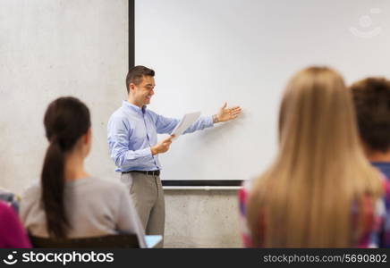 education, high school, technology and people concept - smiling teacher with notepad, laptop computer standing in front of students and showing something on white board in classroom