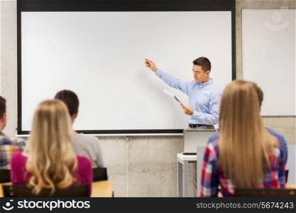 education, high school, technology and people concept - teacher with notepad, laptop computer standing in front of students and showing something on white board in classroom