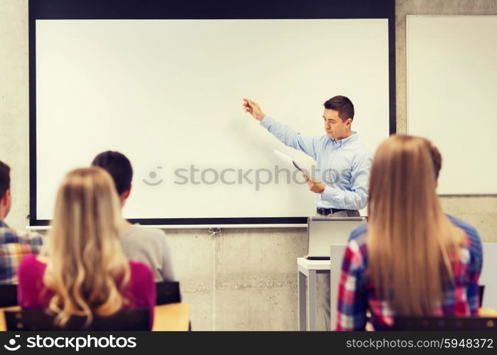 education, high school, technology and people concept - teacher with notepad, laptop computer standing in front of students and showing something on white board in classroom