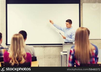 education, high school, technology and people concept - teacher with notepad, laptop computer standing in front of students and showing something on white board in classroom
