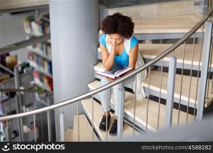 education, high school, university, learning and people concept - african american high student girl reading book sitting on stairs at library