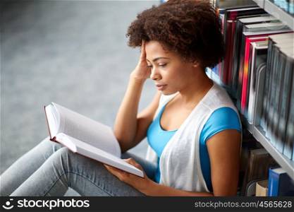 education, high school, university, learning and people concept - african american student girl reading book sitting on floor at library