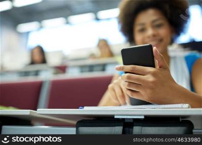 education, high school, university, learning and people concept - close up of happy african student girl with smartphone at lecture hall