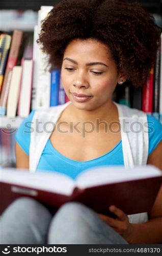 education, high school, university, learning and people concept - close up of african american student girl reading book sitting on floor at library