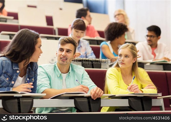 education, high school, university, learning and people concept - group of international students with notebooks writing in lecture hall