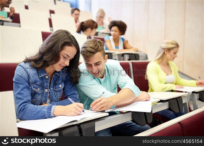 education, high school, university, learning and people concept - group of international students with notebooks writing at lecture hall