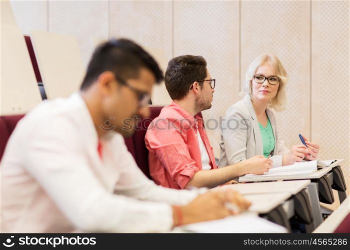 education, high school, university, learning and people concept - group of international students with notebooks in lecture hall and talking