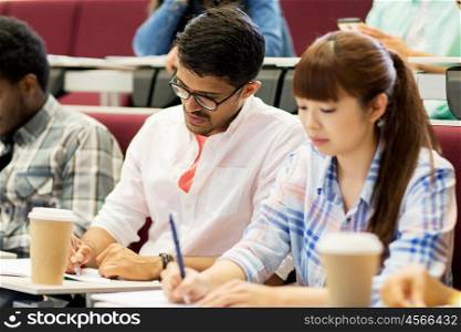 education, high school, university, learning and people concept - group of international students with notebooks and coffee writing test in lecture hall