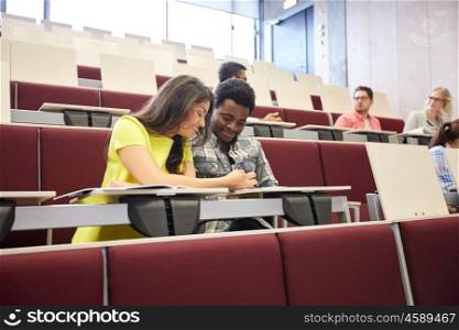 education, high school, university, learning and people concept - group of international students with notebooks writing at lecture hall
