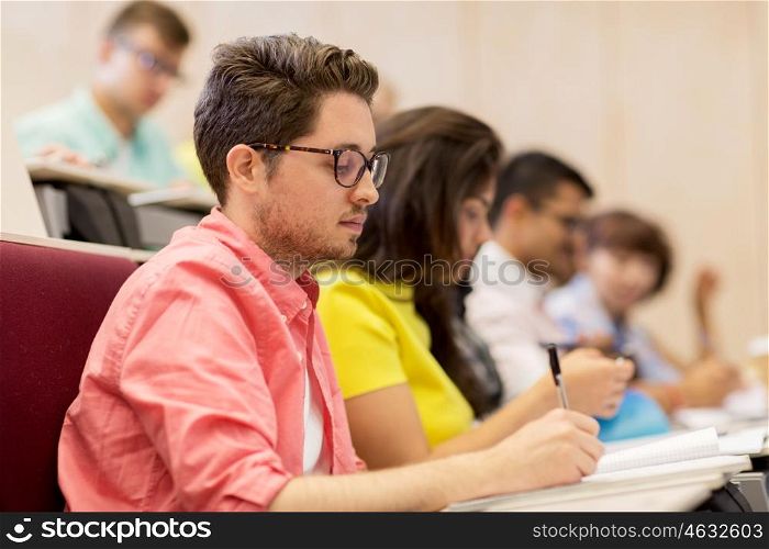 education, high school, university, learning and people concept - group of international students with notebooks writing in lecture hall and talking