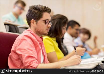 education, high school, university, learning and people concept - group of international students with notebooks writing in lecture hall and talking