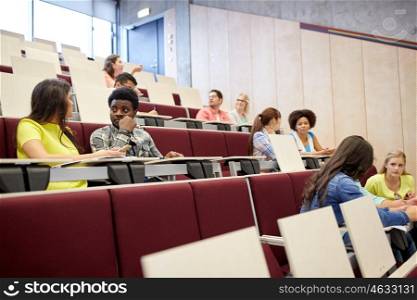 education, high school, university, learning and people concept - group of international students with notebooks talking at lecture hall