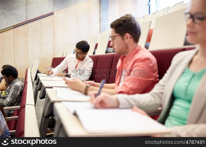 education, high school, university, learning and people concept - group of international students with notebooks writing in lecture hall