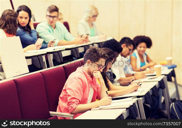 education, high school, university, learning and people concept - group of international students with notebooks writing in lecture hall and talking. group of students with notebooks in lecture hall