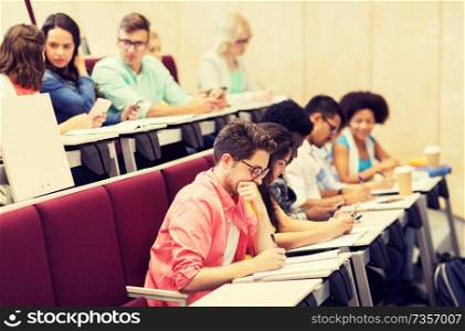 education, high school, university, learning and people concept - group of international students with notebooks writing in lecture hall and talking. group of students with notebooks in lecture hall