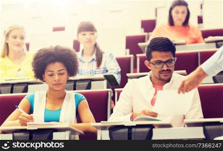 education, high school, university, learning and people concept - group of international students with test in lecture hall. international students with test on lecture