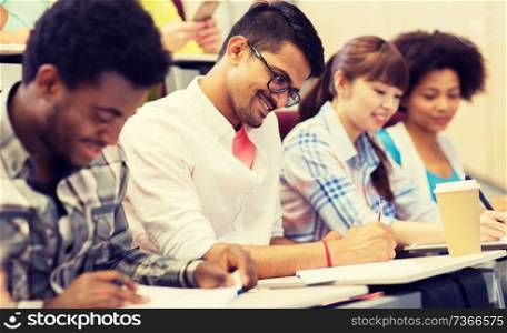 education, high school, university, learning and people concept - group of international students with notebooks and coffee writing test in lecture hall. group of international  students with on lecture 