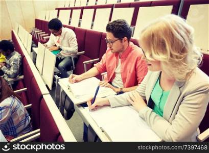 education, high school, university, learning and people concept - group of international students with notebooks writing at lecture hall. group of students with notebooks at lecture hall
