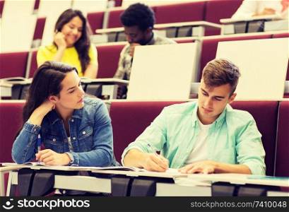 education, high school, university, learning and people concept - group of international students with notebooks writing in lecture hall. group of students with notebooks in lecture hall