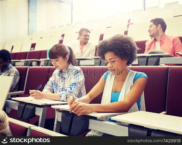 education, high school, university, learning and people concept - group of international students with notebooks writing at lecture hall. group of students with notebooks at lecture hall