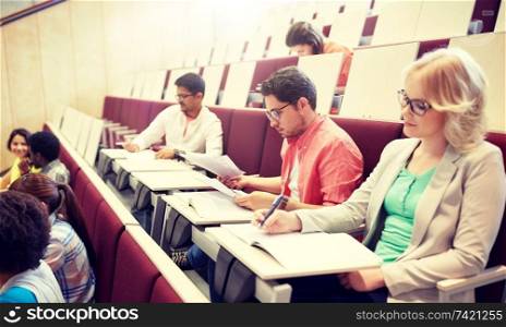 education, high school, university, learning and people concept - group of international students writing test at lecture hall. group of students writing test at lecture hall