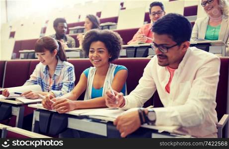education, high school, university, learning and people concept - group of international students with notebooks writing in lecture hall. group of students with notebooks in lecture hall