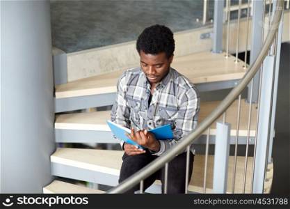 education, high school, university, learning and people concept - happy african american student boy or young man reading book sitting on stairs