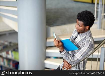 education, high school, university, learning and people concept - happy african american student boy or young man reading book on stairs at library