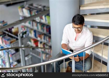 education, high school, university, learning and people concept - happy hindu student boy or young man reading book sitting on stairs at library