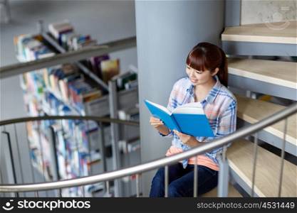 education, high school, university, learning and people concept - happy smiling asian student girl reading book sitting on stairs at library
