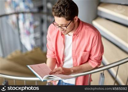 education, high school, university, learning and people concept - happy student boy or young man reading book on stairs at library