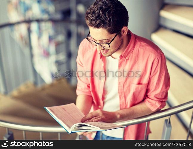 education, high school, university, learning and people concept - happy student boy or young man reading book on stairs at library. student boy or young man reading book at library