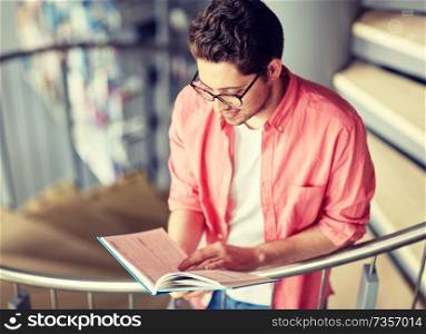education, high school, university, learning and people concept - happy student boy or young man reading book on stairs at library. student boy or young man reading book at library