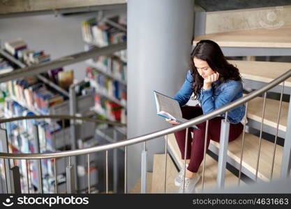 education, high school, university, learning and people concept - student girl reading book sitting on stairs at library